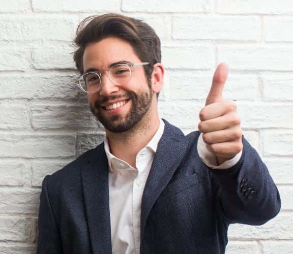 Man in front of white brick wall giving a thumbs up