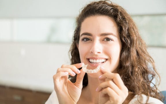 Woman holding a clear aligner in front of her mouth